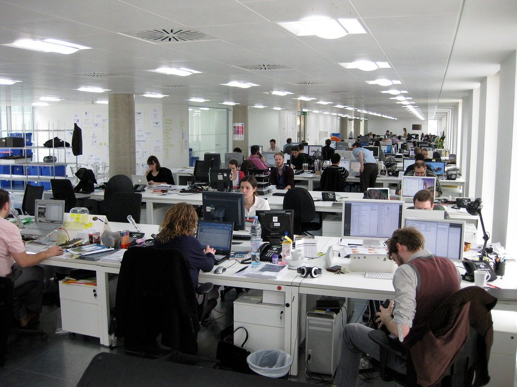 assurance-groupe-vs-delegation Open space dans un bureau avec plusieurs employés au travail, illustrant l'organisation d'un établissement bancaire proposant une assurance de groupe.