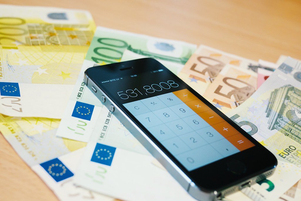 cout-assurance-emprunteur-age-profil Smartphone affichant une application calculatrice posé sur des billets en euros, illustrant le calcul du coût d'une assurance emprunteur selon le profil.