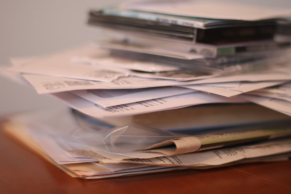 renegocier-assurance-emprunteur-rachat-credit Pile désordonnée de factures et documents papier sur un bureau, illustrant les multiples crédits à regrouper lors d'un rachat de crédit.