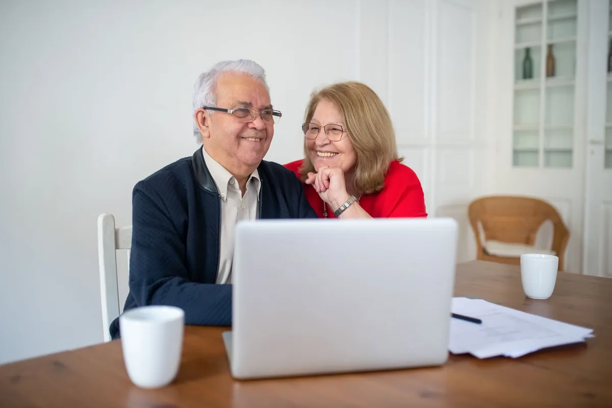 Un couple de personnes âgées lit des documents administratifs assis à une table de cuisine