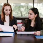 Une personne échange avec un agent d'accueil devant des documents administratifs, dans un bureau de sécurité sociale