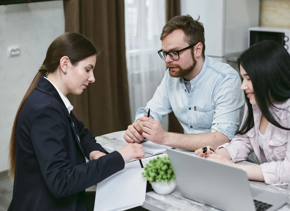 Un couple signe des documents de prêt immobilier face à une conseillère, à un bureau