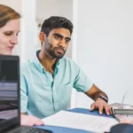 Un couple lit une proposition d'assurance de prêt imprimée, assis face à une conseillère bancaire
