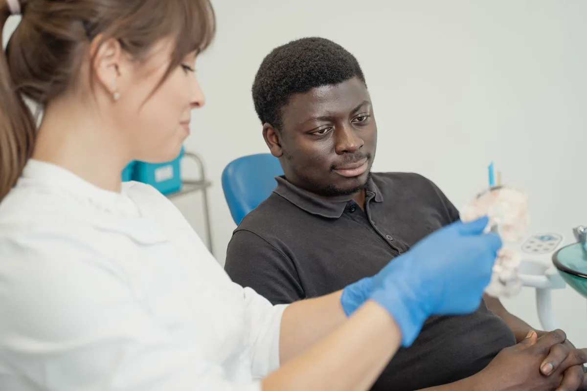 Un chirurgien-dentiste montre une couronne en céramique à une patiente assise dans le fauteuil de son cabinet